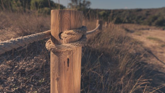 Wooden post wrapped with thick rope on a nature trail, detail shot evoking rustic and outdoor lifestyle. Useful for promoting outdoor adventures, nature preserves, hiking trails, parks, and countryside-themed decor or blogs.