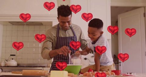 Father and son baking together in kitchen with heart balloon overlay celebrating family bonding