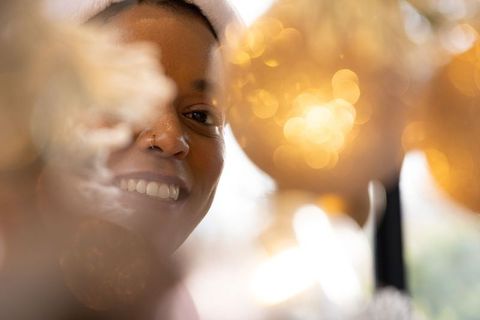 Joyful african american woman smiling wearing headwrap behind golden bokeh ornaments with warm glow