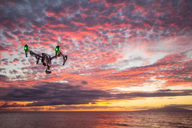 Drone hovering over ocean with vibrant sunset and colorful sky. Suitable for technology ads, travel blogs, photography websites, aerial innovation showcases, and promotional material for drone capabilities.