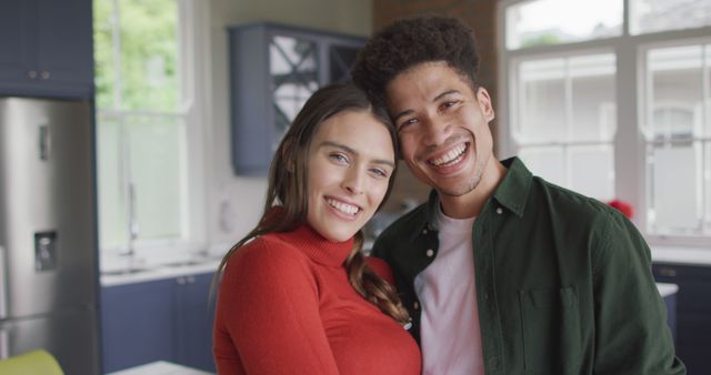 Brightly smiling young couple standing close in a modern kitchen, showcasing affection and happiness. Perfect for themes related to relationships, living together, home life, and multicultural interactions. Ideal for use in lifestyle blogs, home magazines, advertisements, social media campaigns promoting home products or relationship advice.