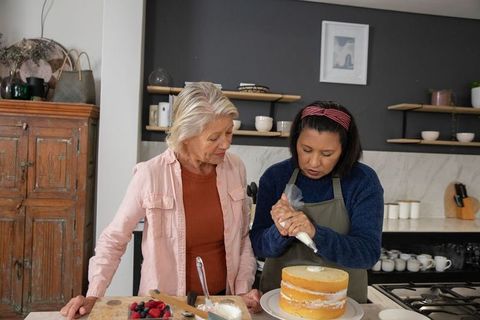 Two women decorating three-layer cake together in cozy kitchen baking collaboration