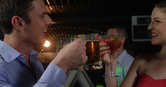 Group of friends enjoying drinks and celebrating at a nightclub. The image depicts a man and woman smiling, toasting with a beer and cocktail in hand. Ideal for content focusing on social gatherings, nightlife, and celebrations.