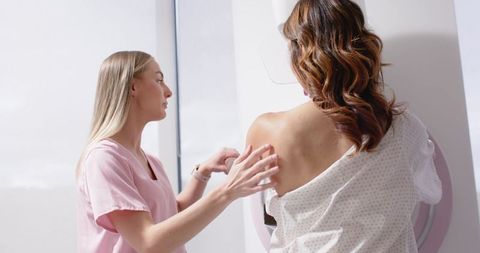 Nurse examining patient preparing for mammogram screening in bright women's clinic room