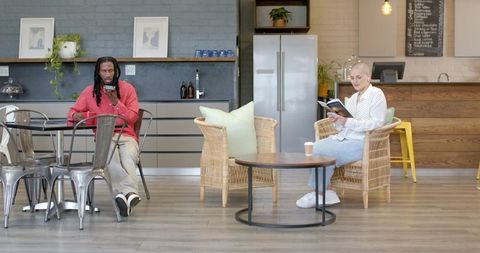 Man and woman relaxing in modern coworking lounge reading paperback and using phone