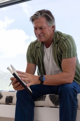 Mature man journaling by window, reflecting with pen and notebook in natural light