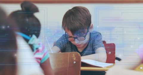 Focused student wearing glasses studying at classroom desk with digital learning overlays