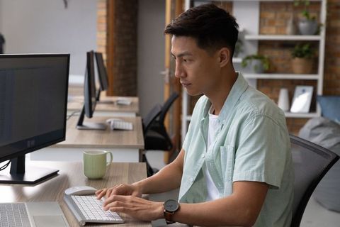 Focused Asian Professional Typing in Modern Open-Plan Office