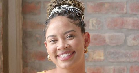 Confident young woman smiling by sunlit brick wall