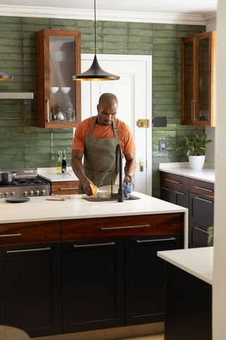 Washing stainless bowl on island by african american man wearing apron in modern kitchen