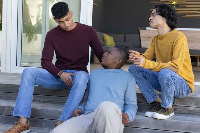 Multiracial teen friends relaxing on porch steps sharing snack and friendly conversation