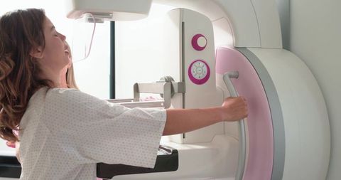 Woman undergoing mammogram screening for breast cancer in modern pink mammography unit