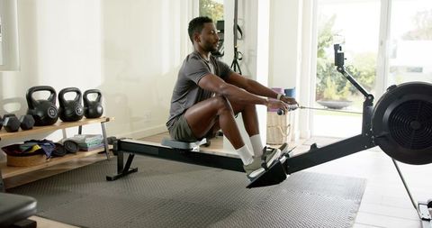 African american man rowing on home rowing machine during strength cardio workout