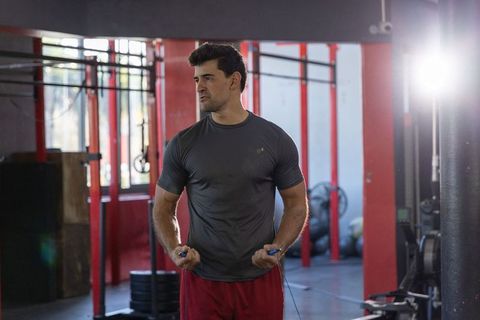 Focused athlete preparing jump rope while standing in gym with weights and backlit windows