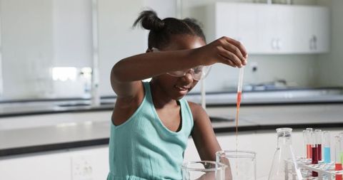 Young female student conducting colorful chemistry experiment with pipette in school lab