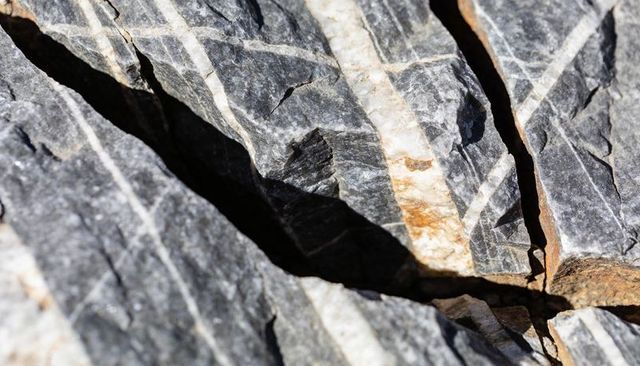 Fractured gray bedrock revealing white quartz veins and rust-stained fissures on crag