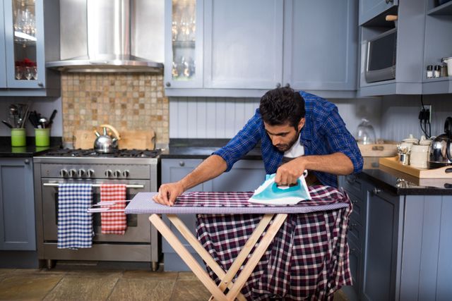 Young man ironing shirt on board in kitchen at home