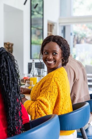 Smiling woman in yellow sweater chatting with friends at modern kitchen counter