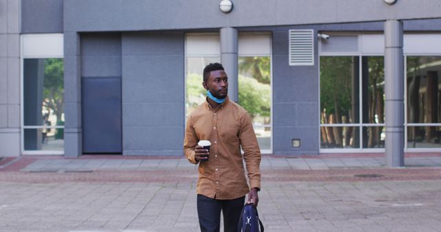 Casual scene of a man holding a coffee cup while walking outside an office building. Ideal for use in business, lifestyle, and casual theme projects, as well as urban setting and morning routine visuals.