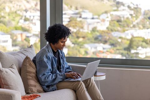 African american man working remotely on laptop in sunlit living room with hill view