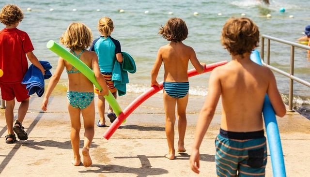 Children walking toward sea carrying bright pool noodles on beach ramp summer friendship