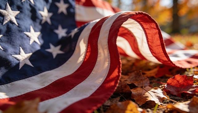 Close-up waving american flag draped over autumn leaves catching warm golden sunlight