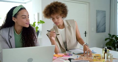 Two african american women collaborating on beauty moodboard in bright home office workspace