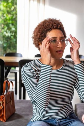Woman adjusting glasses in sunlit dining room with handbag