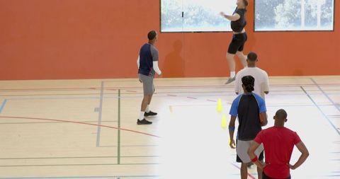 Basketball players practicing vertical jump drill with cones on bright indoor court