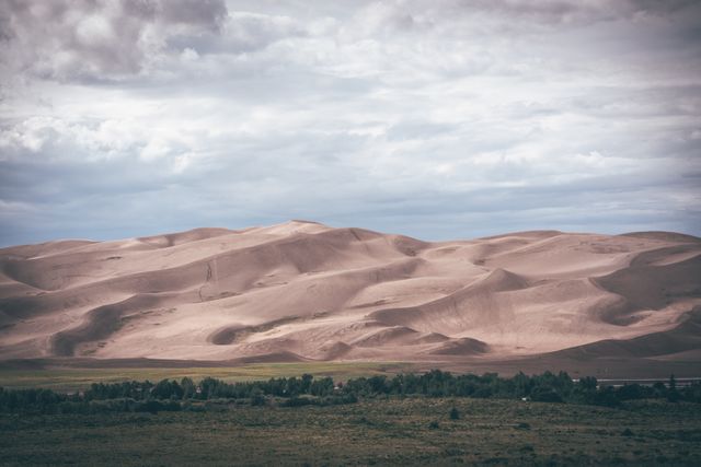 Desert sand dunes stretch under a cloudy sky, creating a contrasting view of arid land and atmospheric weather. Ideal for illustrating travel, adventure, and natural exploration themes in blogs, articles, posters, and educational materials related to geography or climate.