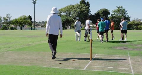 Cricket umpire walking toward pitch with batsmen and teammates during practice match