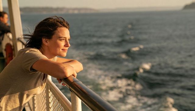 Young woman leaning on ferry railing enjoying golden hour ocean view and peaceful reflection