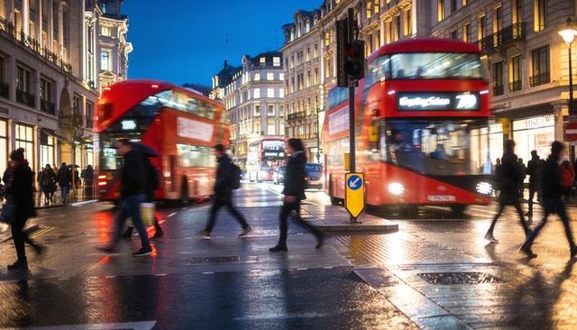 Rainy london dusk with moving red double-decker buses and pedestrians on wet crossing