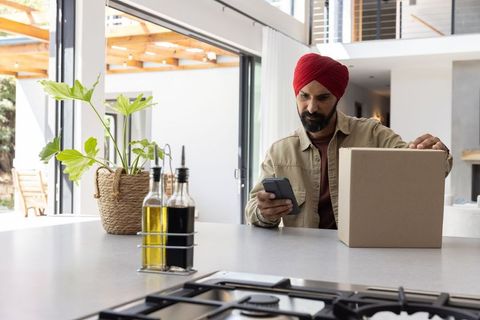 Middle-eastern man with smartphone and parcel in modern kitchen