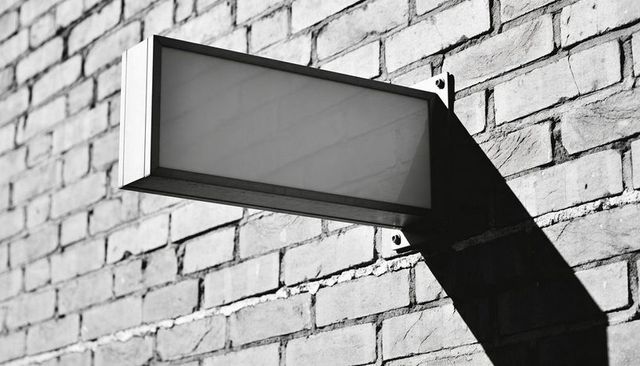 Rectangular projecting metal sign on brick wall casting bold diagonal shadow