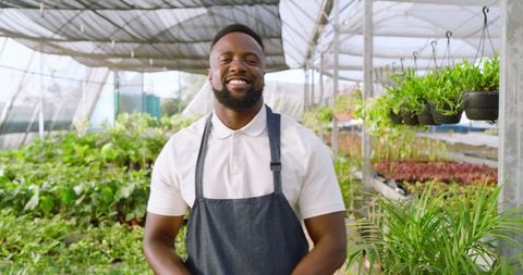 Smiling Gardener in Greenhouse Wearing Denim Apron Among Diverse Plants
