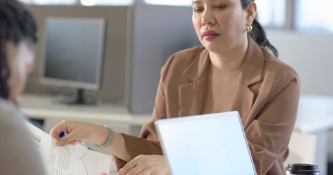 Diverse coworkers reviewing charts during office collaboration with woman in brown blazer