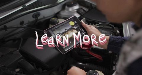 Female technician holding tablet inspecting car engine bay with diagnostic jump leads