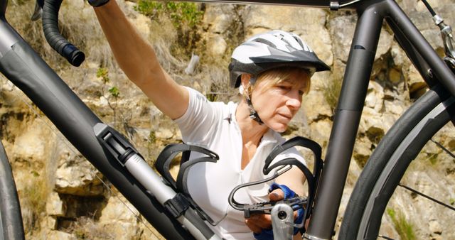 Depicts a female cyclist in a helmet and cycling gear repairing a bike outdoors. Suitable for use in articles or advertisements focused on outdoor activities, cycling, bike maintenance, female athletes, and active lifestyles.