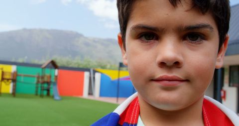 Schoolboy Wrapped in American Flag Standing in Vibrant Playground