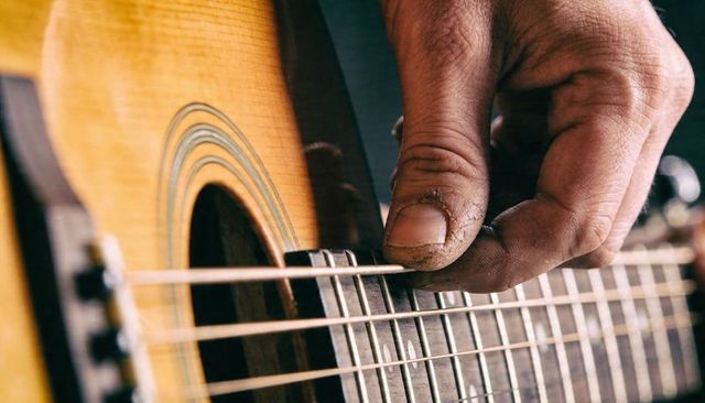 Close-up Showing Rough Hand Plucking Acoustic Guitar Strings on Wooden Fretboard