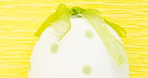 Polka dot easter egg with green bow on bright yellow background
