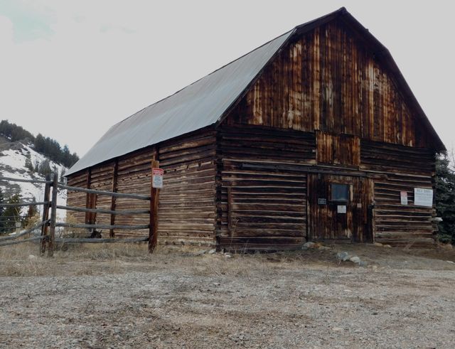 Old rustic wooden barn in countryside. Weathered wood and wooden fence add to charm. Ideal for agriculture, farming, rural lifestyle themes, or historical preservation projects.