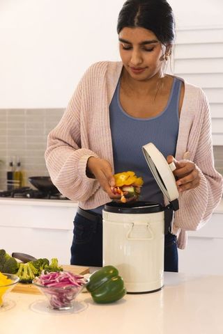 Woman Adding Vegetables to Kitchen Compost Bin, Embracing Sustainability