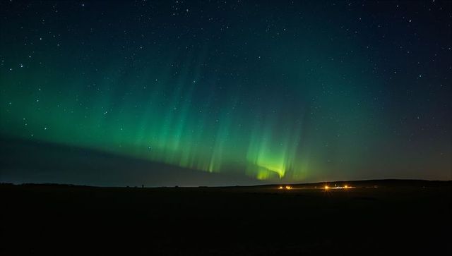 Aurora Borealis dancing over rural moorland with distant farm lights and starry night sky