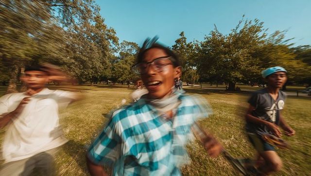 Teens sprinting through park with skateboard, motion blur showing energy and friendship