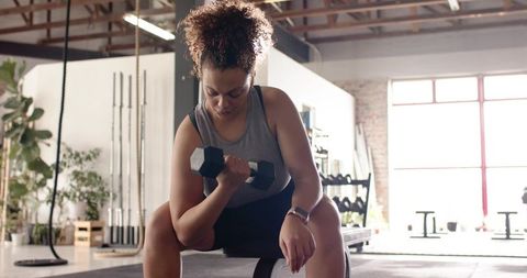 Determined woman performing seated dumbbell curl on bench in modern minimalist gym
