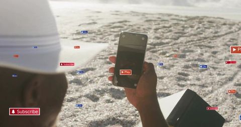 Man holding smartphone on sunny beach with floating social media icons and play button