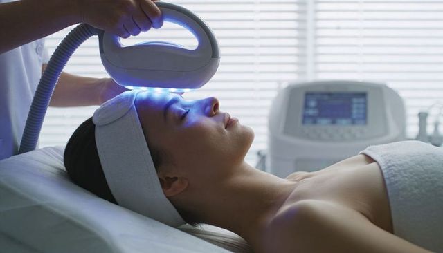 Asian woman receiving blue led facial therapy with professional device in medical spa