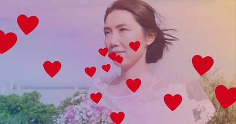 Bride standing on rooftop garden holding pale pink bouquet with floating red hearts